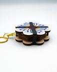 Side view of the flower press keychain showing its wood layers and black elastic bands