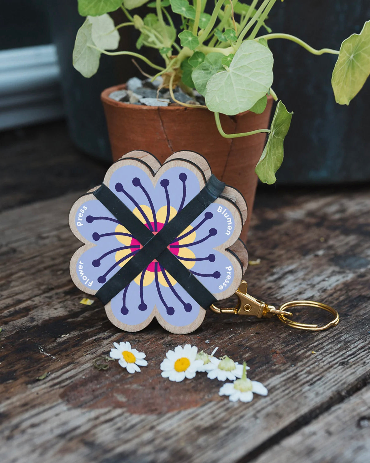 Studio Wald Periwinkle flower press keychain on a garden table with daisies