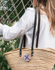Flower press keychain clipped to the handle of a woven straw tote bag