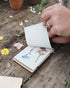 Hand lifting a page of a Studio Wald flower press to show pressed wildflowers
