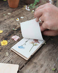 Hand lifting a page of a Studio Wald flower press to show pressed wildflowers