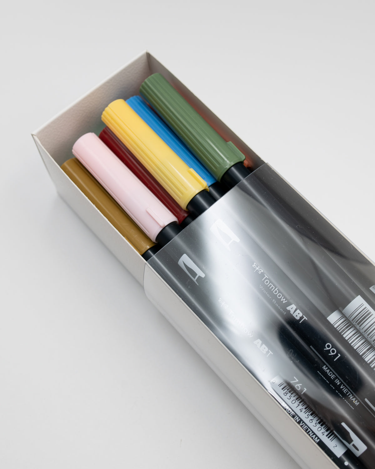 Open box of Tombow dual brush pens in pink, yellow, blue and green on a white background.