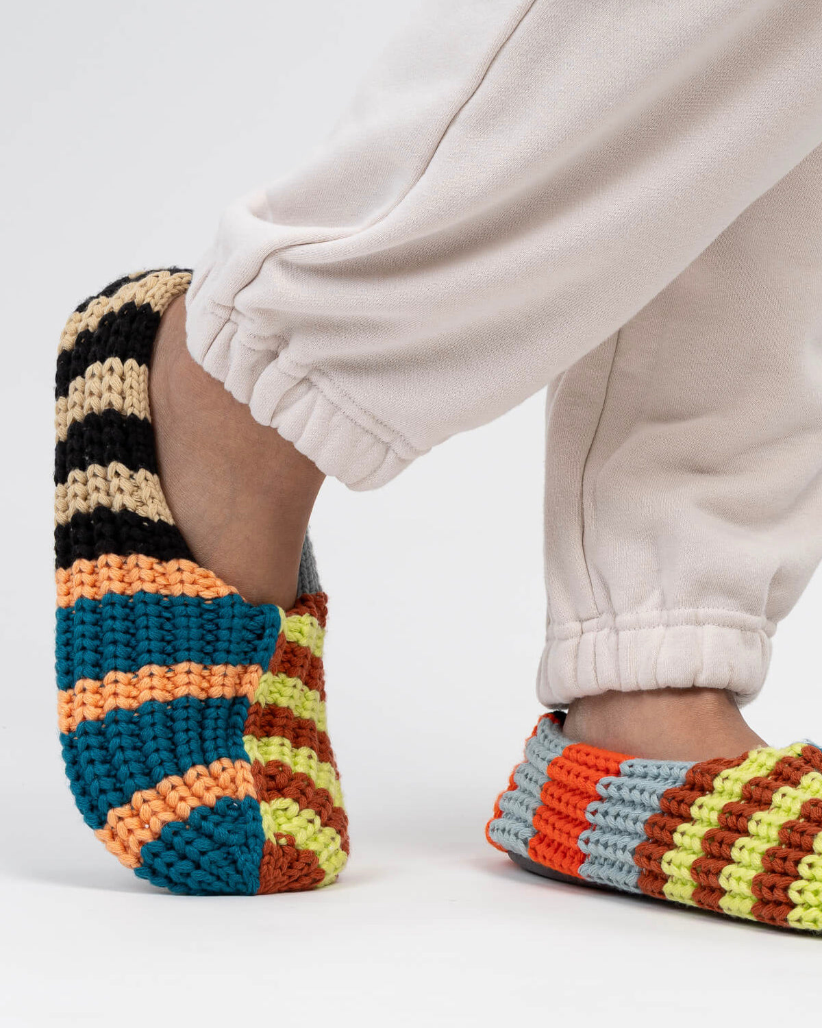 Side view of the striped knit house slippers worn with cream sweatpants