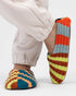 Person in cream joggers wearing Verloop knit house slippers in bold multicolor stripes