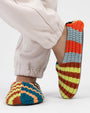 Person in cream joggers wearing Verloop knit house slippers in bold multicolor stripes