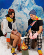 Teen girl and teen boy wearing Verloop grid knit beanies, mismatch scarves, knit house socks and striped mittens, pretending to roast marshmallows over a faux-campfire.