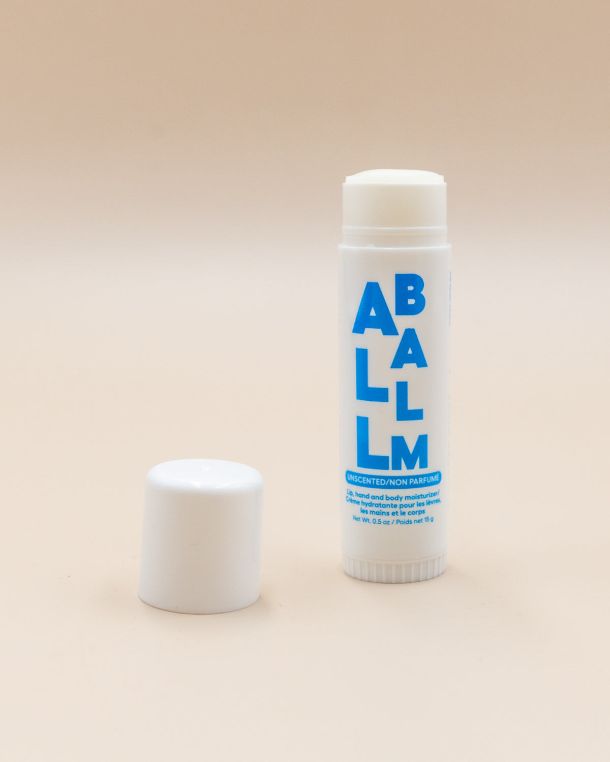 Uncapped Zizia All Balm stick beside its cap on a beige background