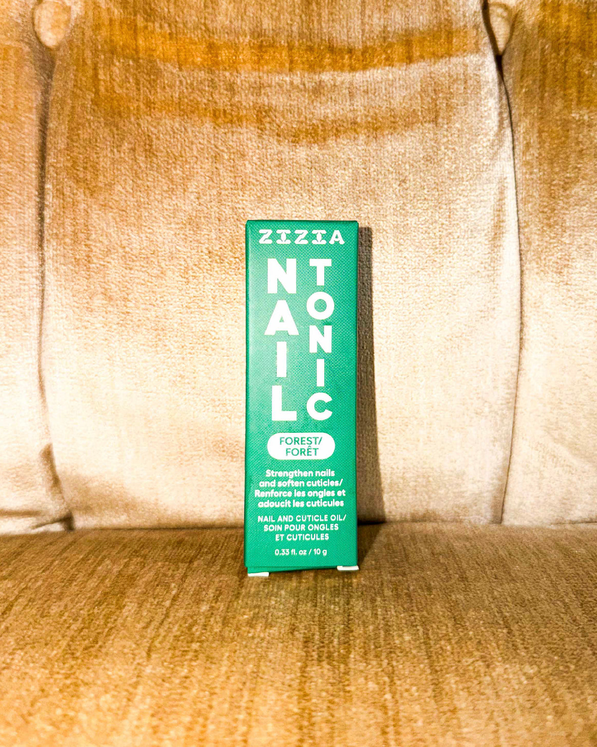 Zizia Nail Tonic box standing on a velvety gold armchair