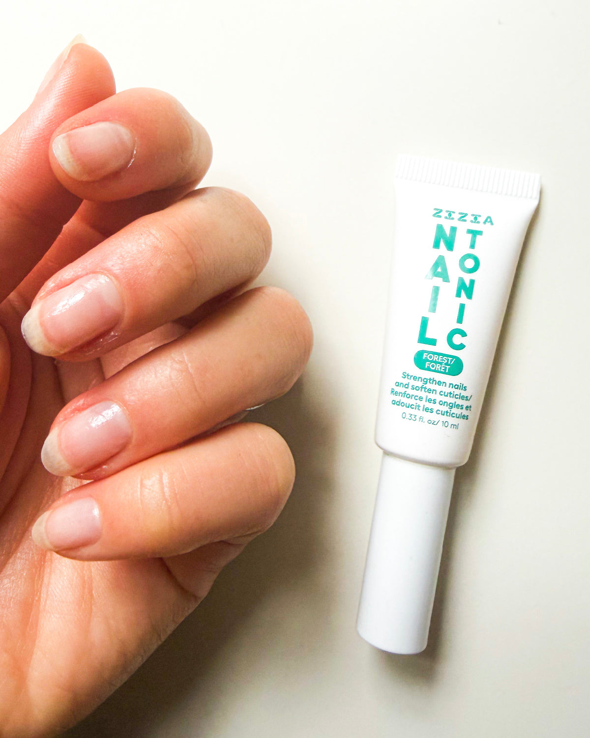Hand with bare, healthy nails holding a tube of Zizia Nail Tonic