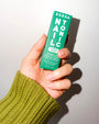 Hand in a green sweater holding the Zizia Nail Tonic box in green and white