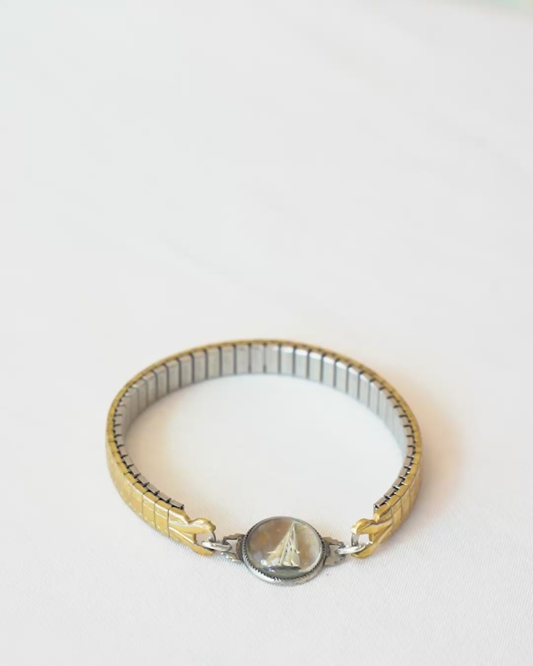 A person trying on a gold-toned vintage watch band bracelet with delicate hand painted design in a glass charm