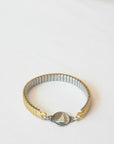 A person trying on a gold-toned vintage watch band bracelet with delicate hand painted design in a glass charm