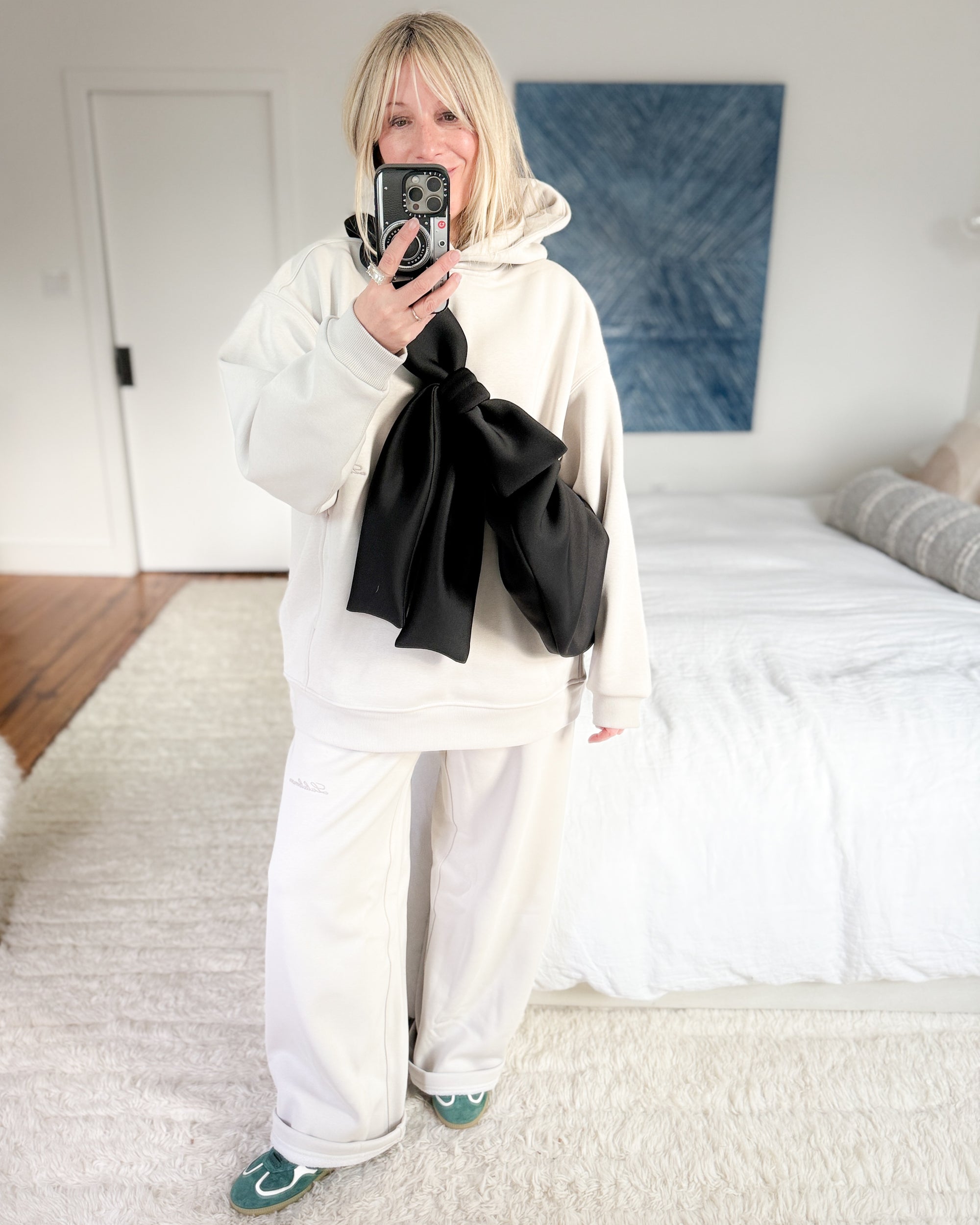 Casual winter outfit with a black bow crossbody bag worn over lululemon's white hoodie and matching wide-leg sweatpants.
