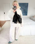 Casual winter outfit with a black bow crossbody bag worn over lululemon's white hoodie and matching wide-leg sweatpants.