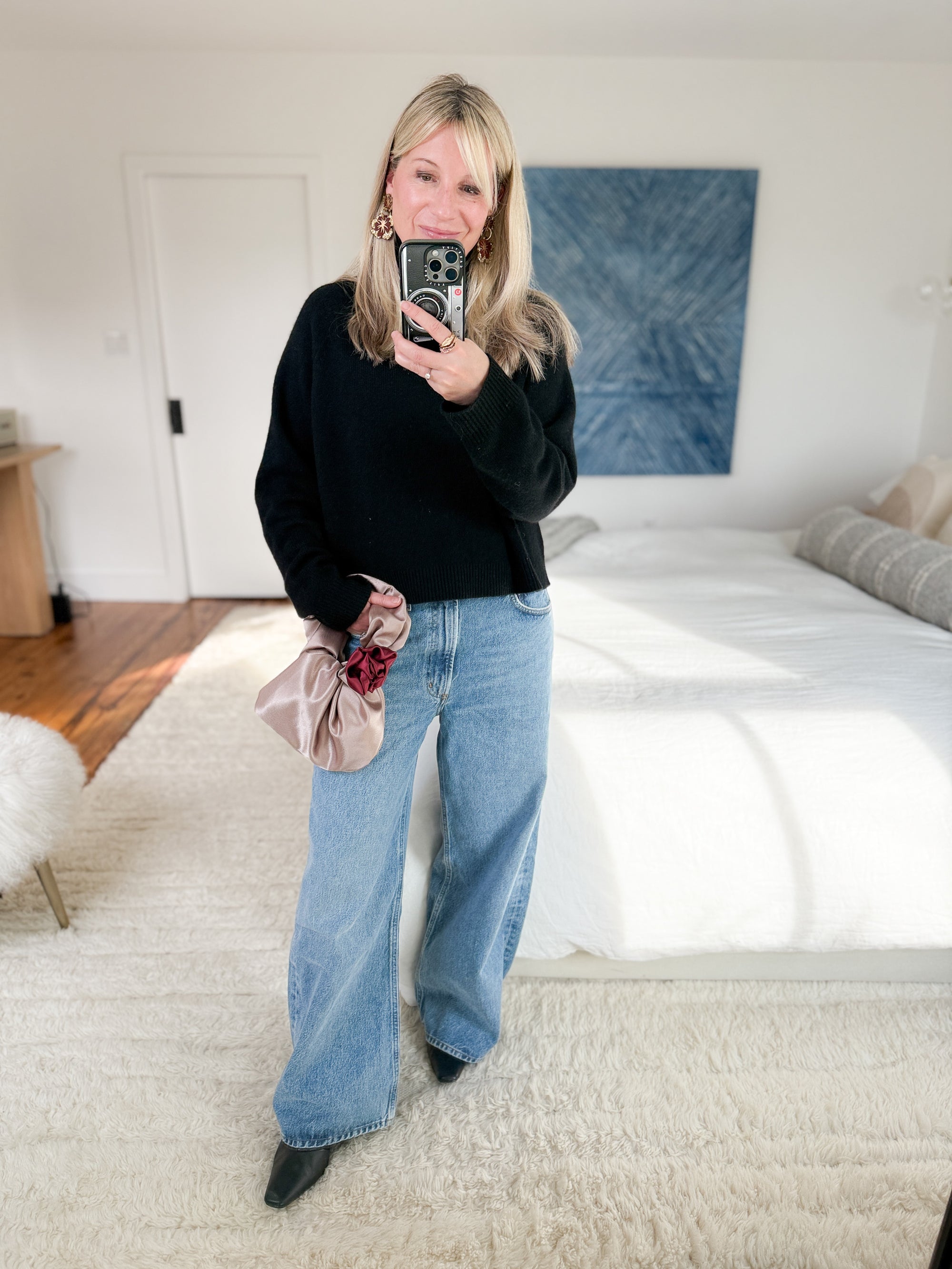 Woman wearing champagne rosette clutch crossbody with black sweater and jeans.