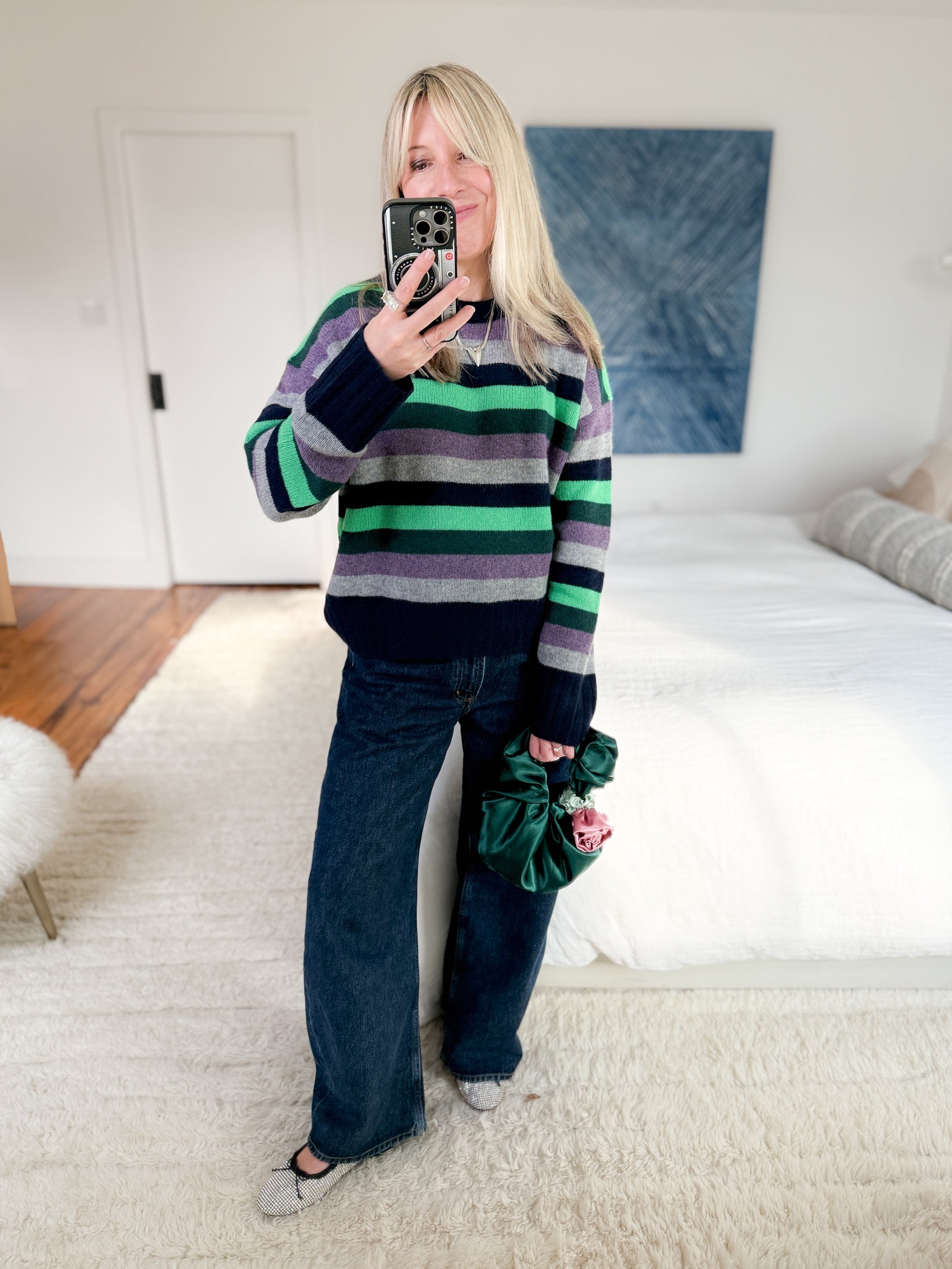 Woman styling emerald rosette clutch bag with striped sweater and wide-leg jeans.